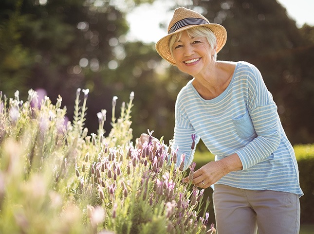 Woman in striped shirt and straw hat touching flowers outside