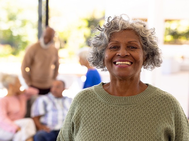 Woman in green sweater with short grey hair smiling with friends blurry in the background