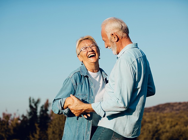 Older man and woman wearing denim outside laughing together