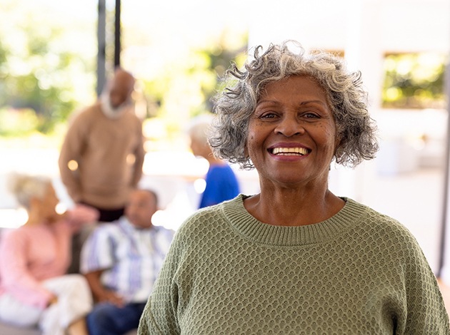 Woman with gray hair in green sweater smiling with friends blurry in the background