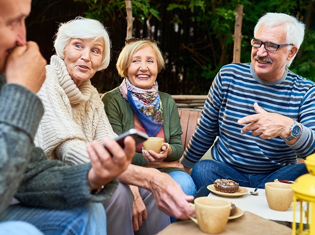 Four older adults around a table talking over coffee and donuts