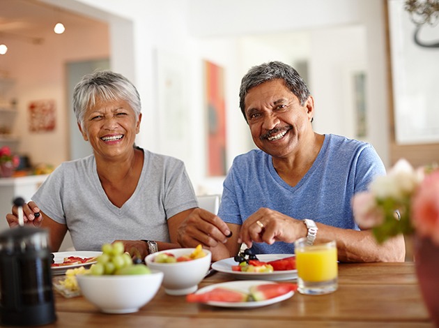 Man and woman with gray hair eating fruit for breakfast at a wooden table