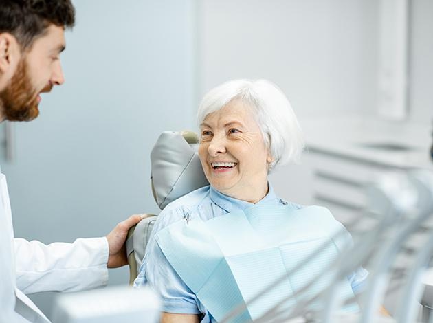 Woman with white hair in dental chair smiling at dentist in white coat